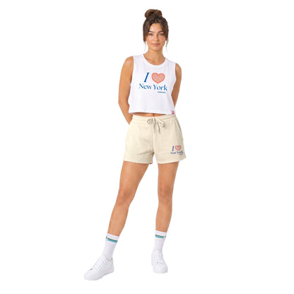A woman modeling a white sleeveless crop top and cream-colored sweat shorts, both featuring a 'I [heart] New York' graphic. She is wearing white sneakers and striped socks against a solid white background.
