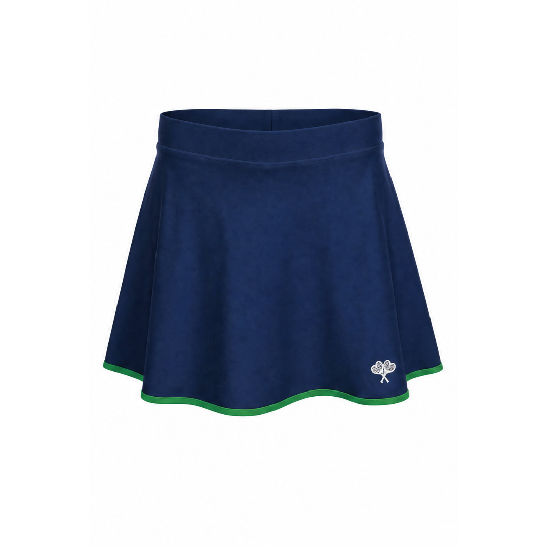 A navy blue athletic skort with a thin green trim along the hem and a small white embroidered clover logo on the lower left side, shown against a plain white background.