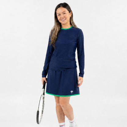 A woman modeling a navy blue long-sleeve tennis dress with green trim, holding a tennis racket against a plain white studio background.