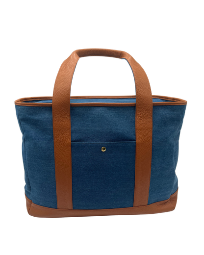 A blue denim tote bag with brown leather handles, trim, and base, shown against a plain white background.
