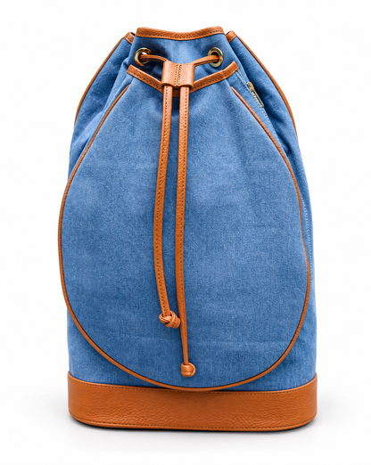 A blue denim drawstring backpack with tan leather trim and a matching tan leather base, shown against a plain white background.