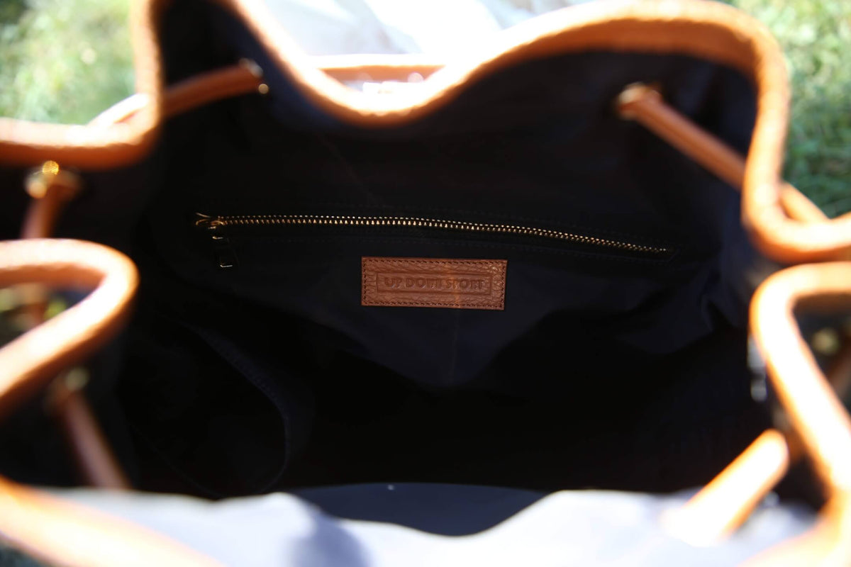 Close-up view from inside a black bucket bag with tan leather trim and drawstring handles, showing a small brown interior label that reads 'UP DOWN SPORT'.